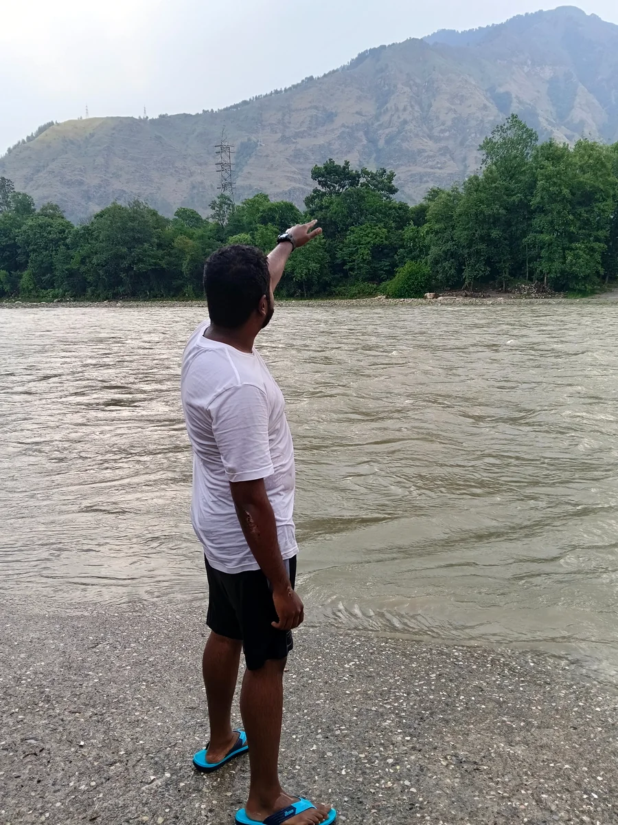 A creator standing near a river and pointing toward distant mountains.